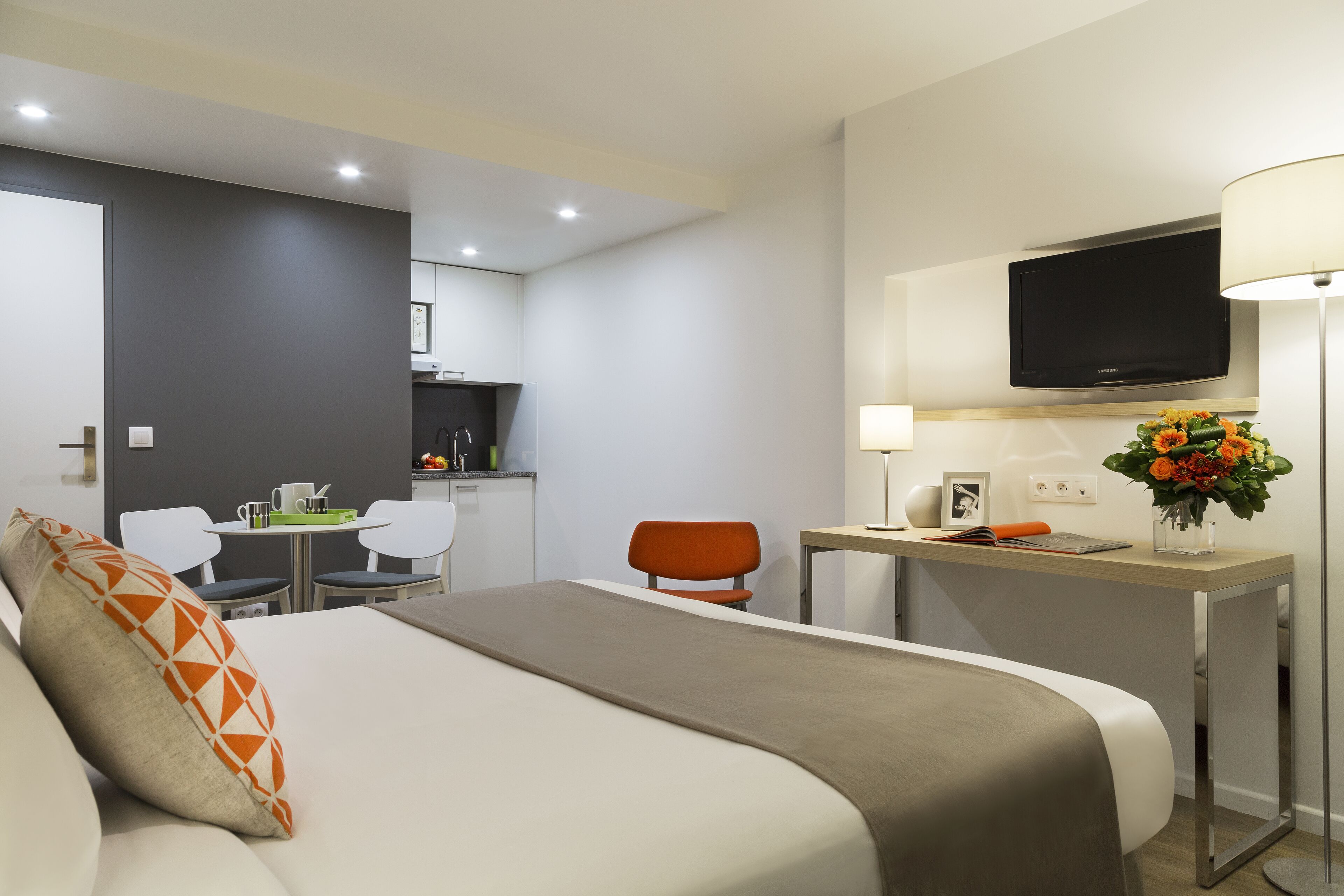Een hotelkamer met een bed, een bureau, een stoel, een televisie en een kleine kitchenette.