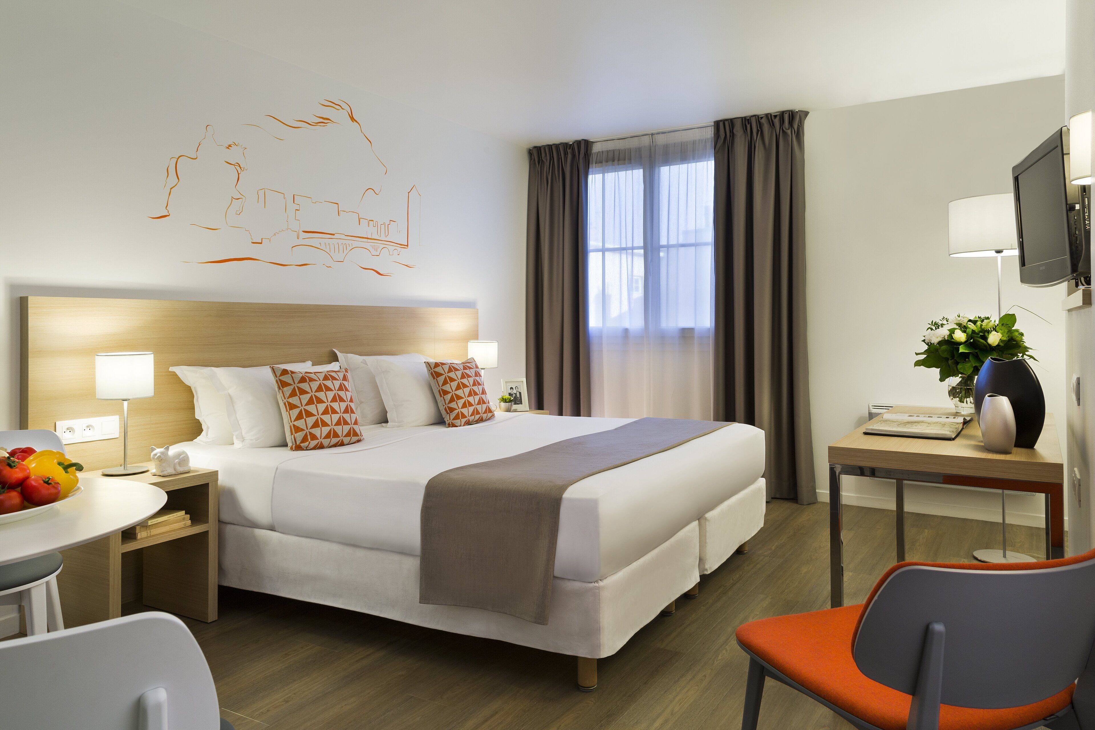 A hotel room with a large bed, bedside tables, a desk, a chair, and a TV.