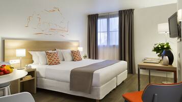 A hotel room with a large bed, bedside tables, a desk, a chair, and a TV.