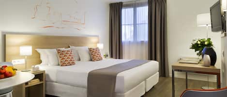 Una habitación de hotel con una cama grande, mesitas de noche, un escritorio, una silla y un televisor.