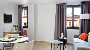 A hotel room with a dining area, a sofa, a TV, and a window with curtains. - Citadines Presqu'île Lyon (Lyon)