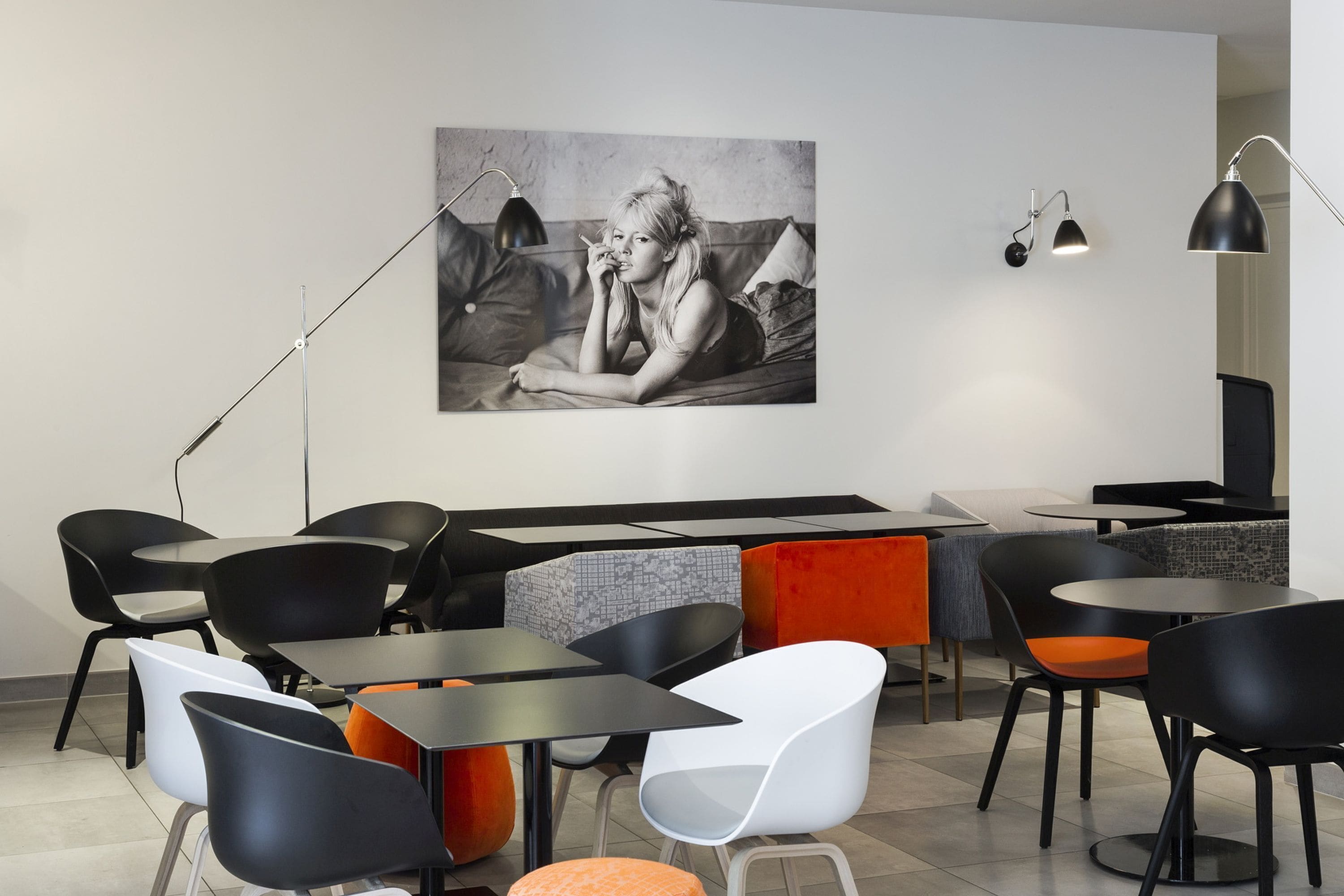 Un café moderne avec des chaises et des tables noires et blanches, et une grande photographie en noir et blanc accrochée au mur.