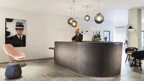 A modern reception area with a curved reception desk, a single chair, and a potted plant. - Citadines Presqu'île Lyon (Lyon)