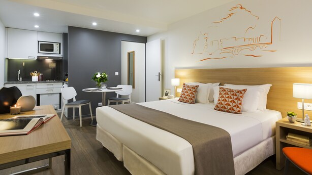 A hotel room with a large bed, a desk, a chair, a small table, a microwave, and a kitchenette. - Citadines Presqu'île Lyon (Lyon)