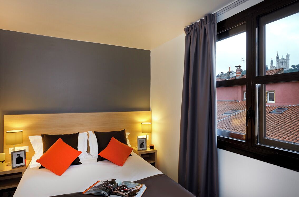 Une chambre d’hôtel avec un lit, des tables de chevet et une fenêtre donnant sur un paysage urbain.
