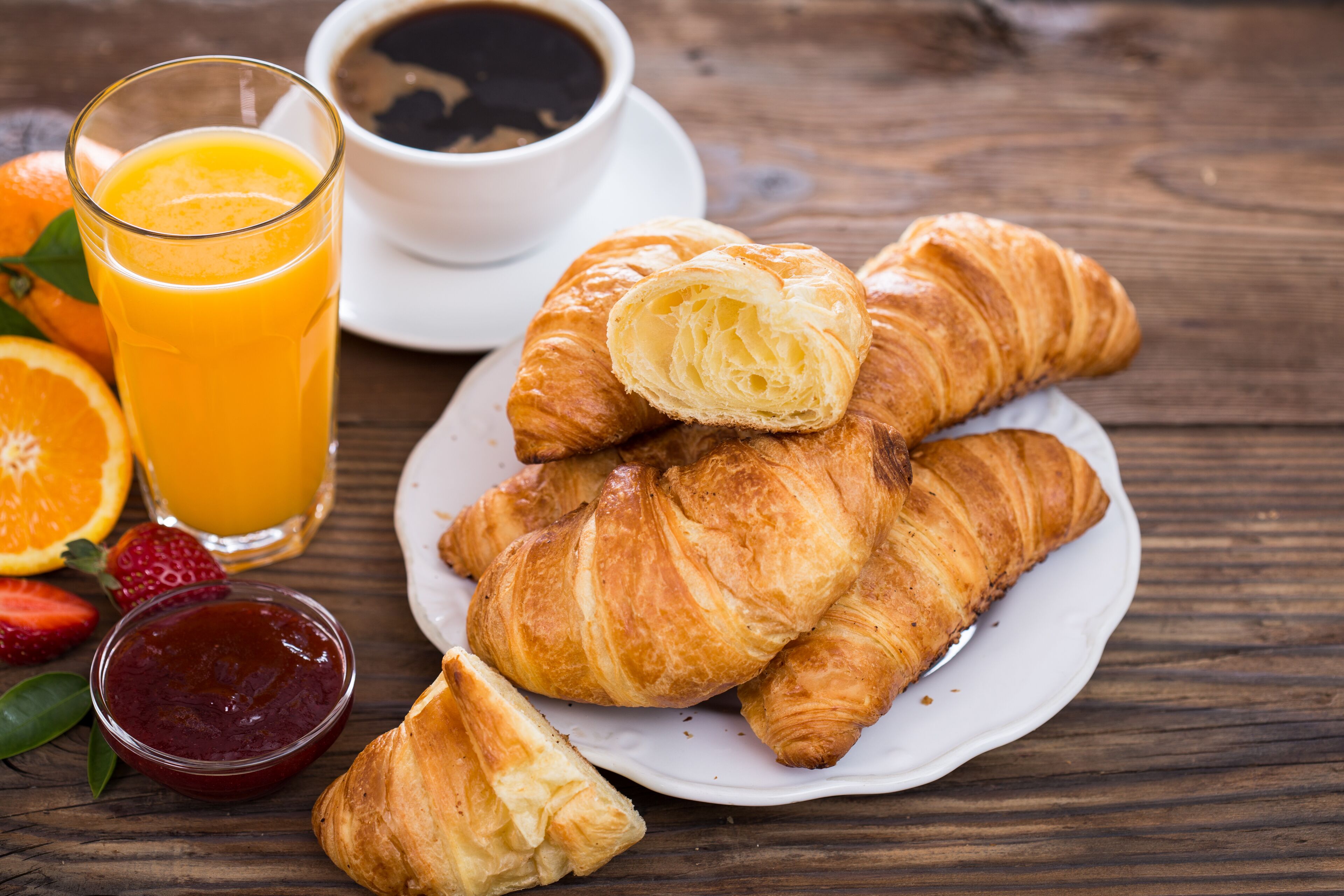 A breakfast setting with croissants, orange juice, coffee, and strawberries.