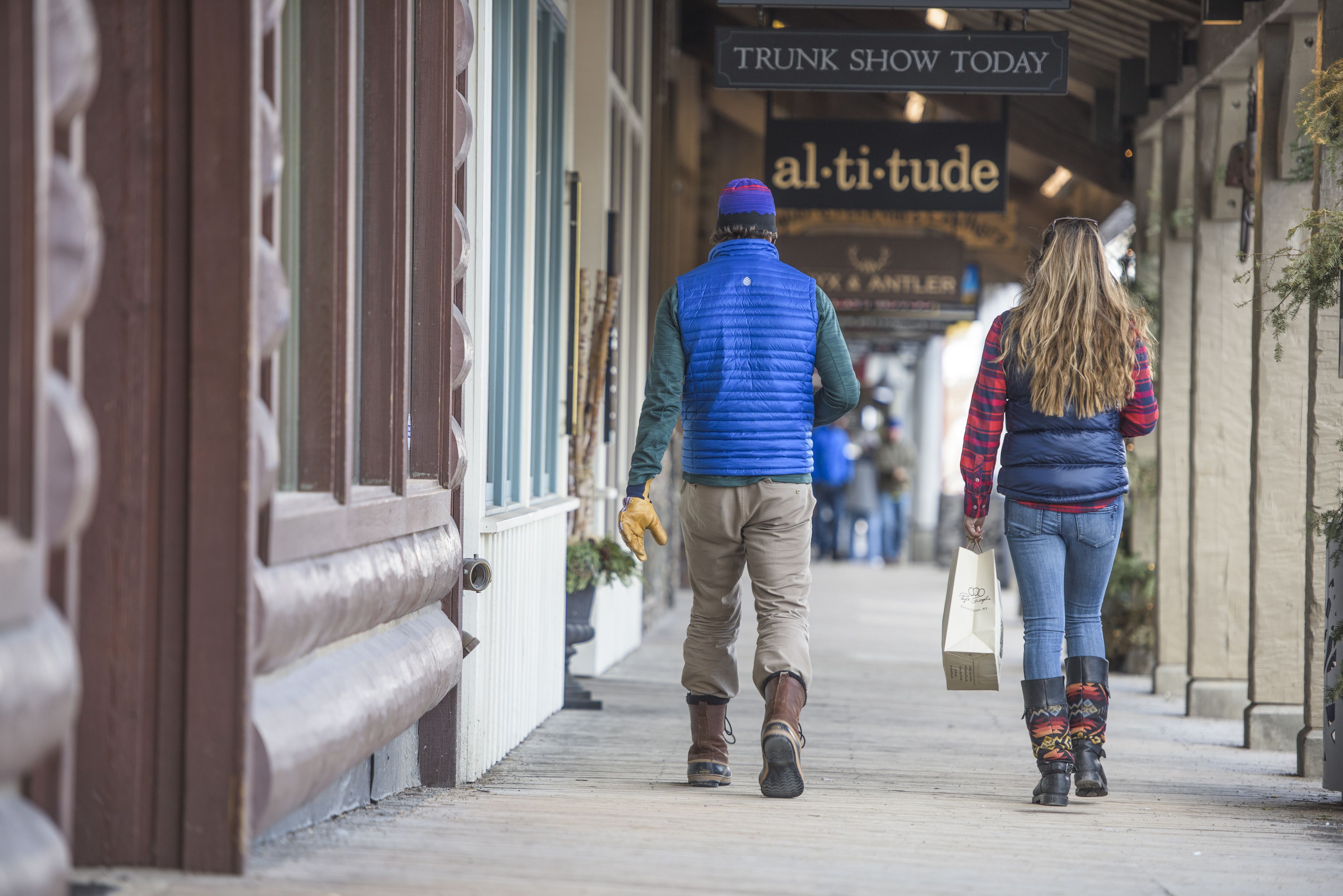 Un pasillo con tiendas y carteles, incluyendo 'TRUNK SHOW TODAY' y 'al-ti-tude'.