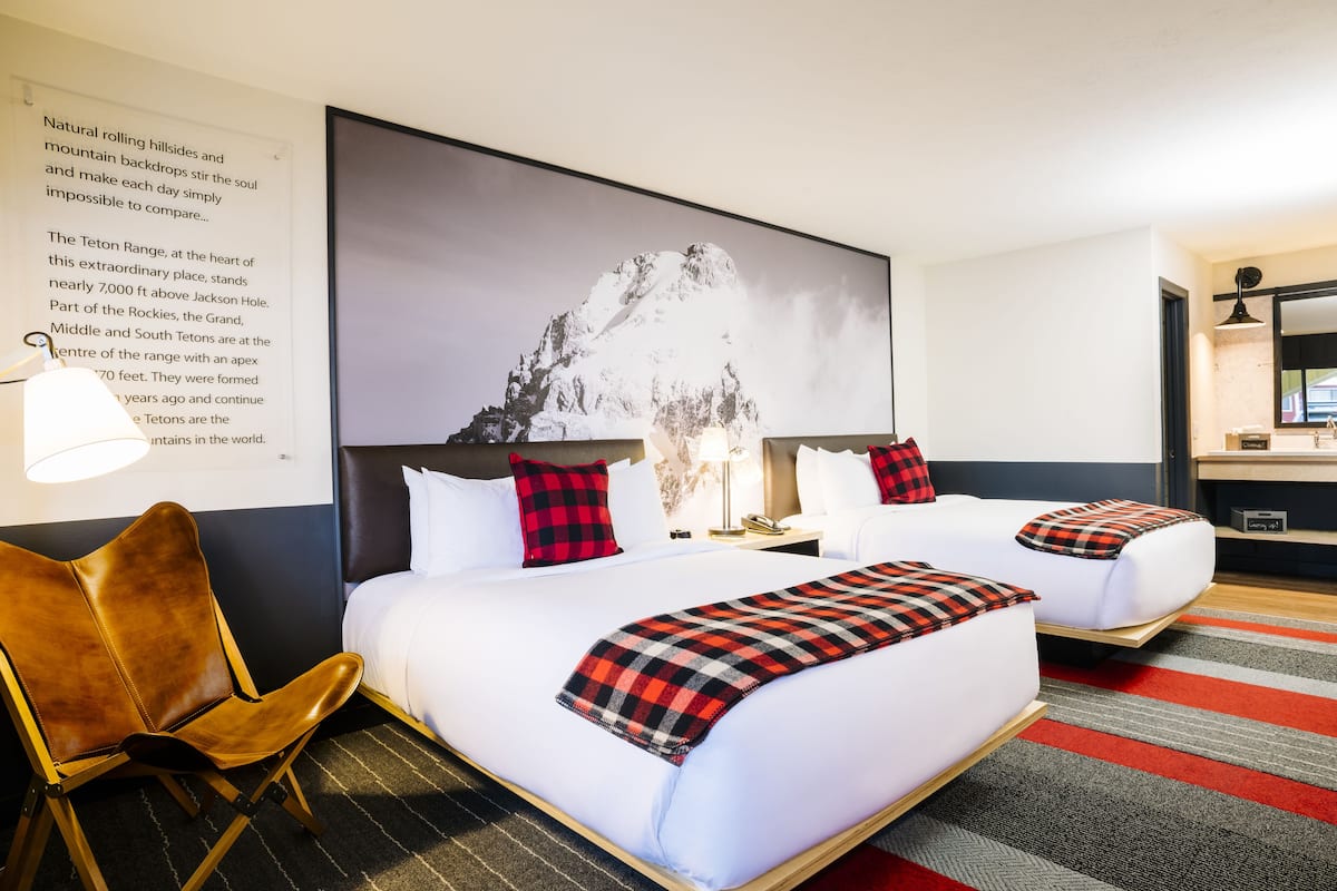 A hotel room with two beds, a large mountain image on the wall, a brown leather chair, and a striped carpet.
