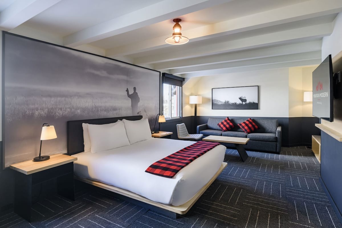 A hotel room with a bed, a sofa, a desk, a lamp, a TV, and a painting on the wall.