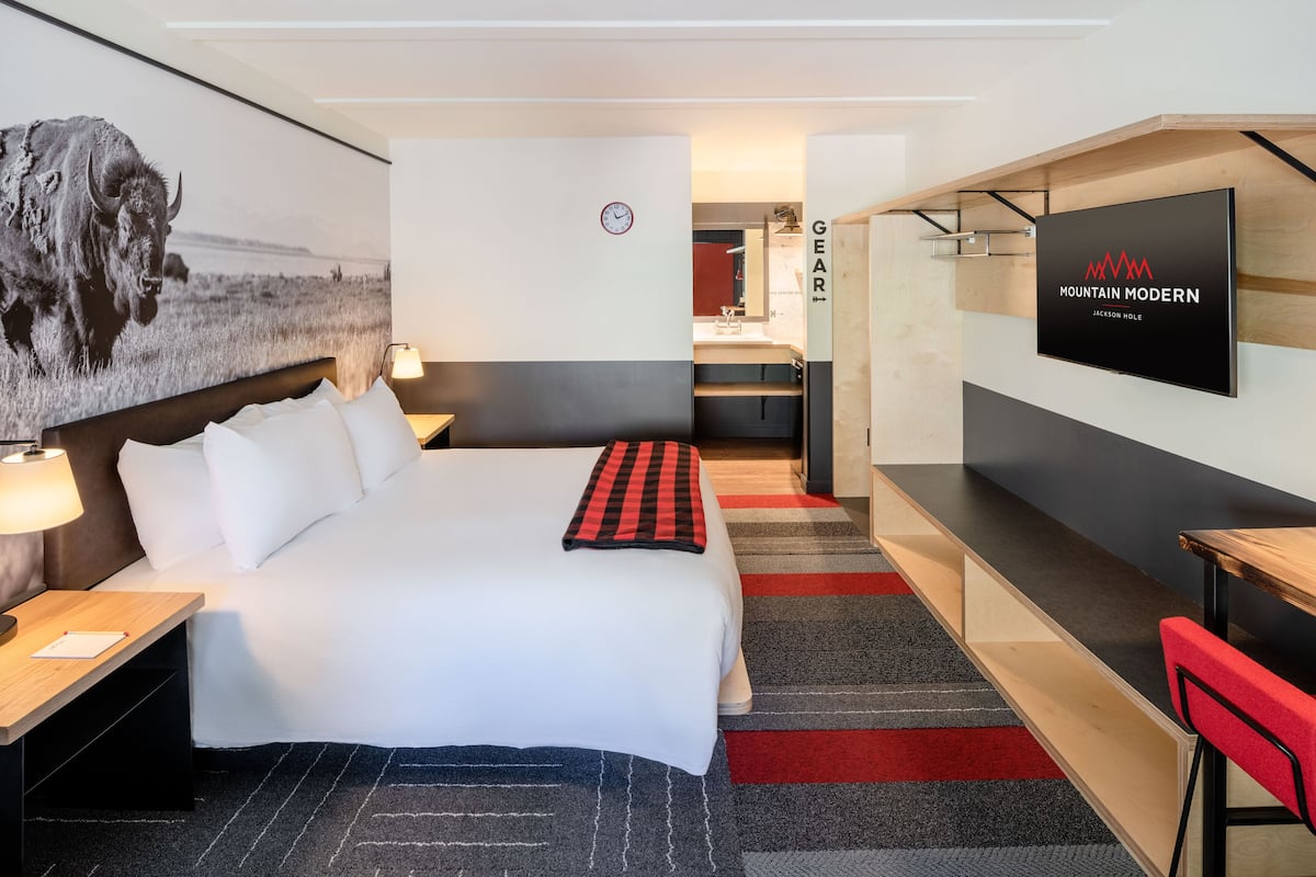 A hotel room with a bed, bedside tables, a TV, a desk, and a red chair.
