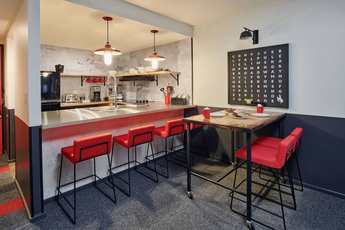 A modern kitchen with a bar area, red bar stools, and a wall-mounted crossword puzzle.