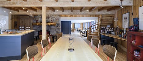 Un vaste espace dédié à la salle à manger, avec une longue table, des chaises en bois et un îlot central doté d’un comptoir.