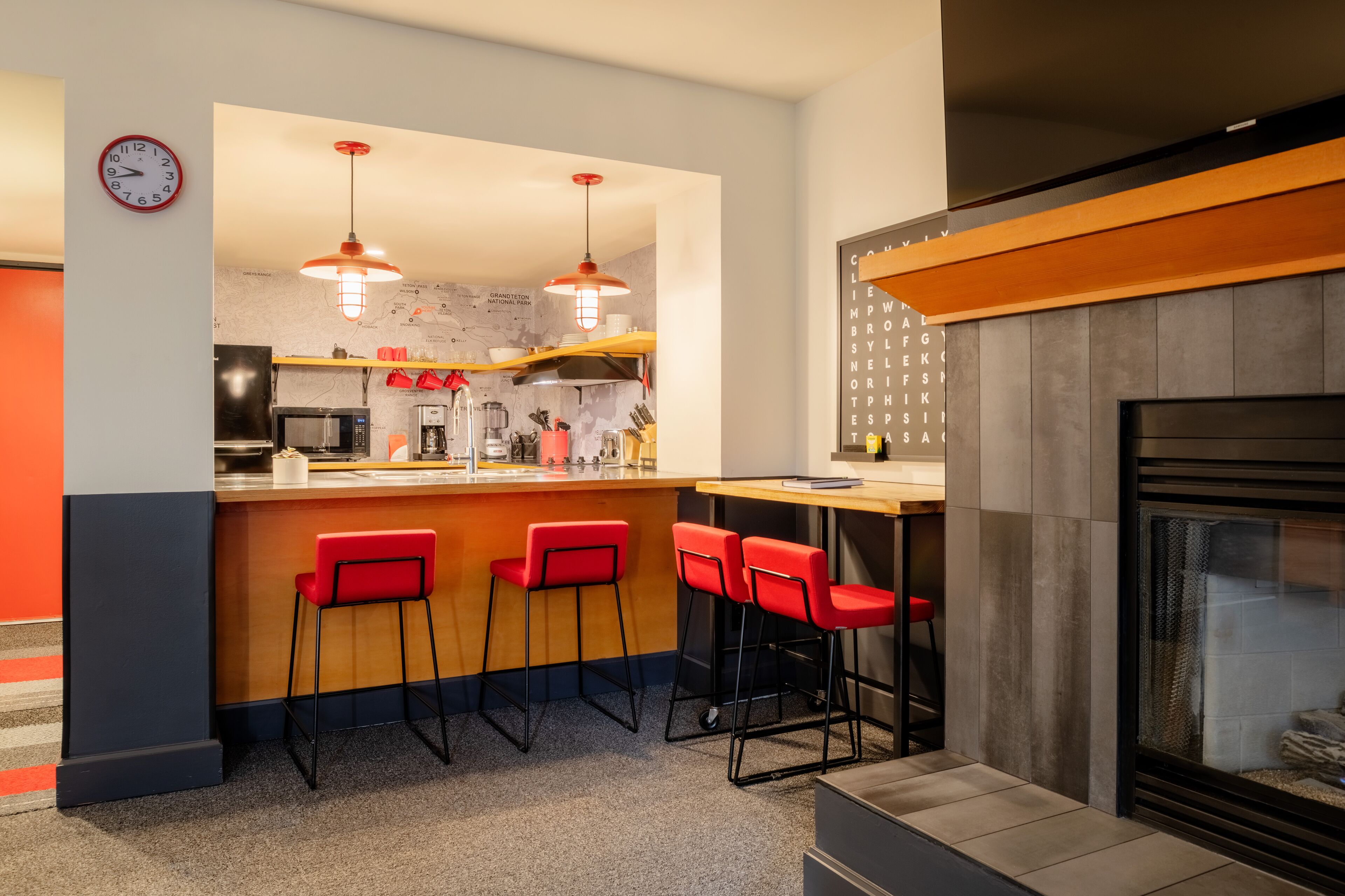 Une cuisine moderne avec un coin bar, des tabourets de bar rouges et une horloge au mur.