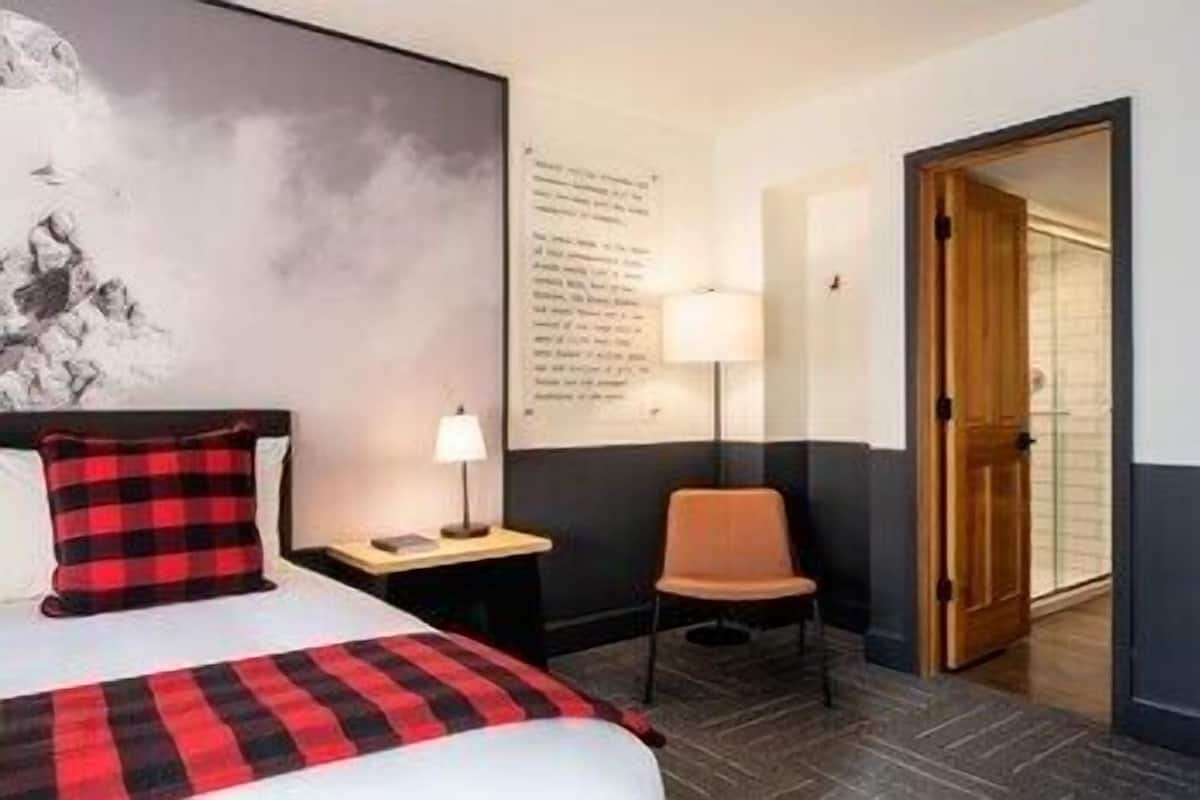 A hotel room with a bed, a chair, a nightstand with a lamp, a wall with text, and a door.