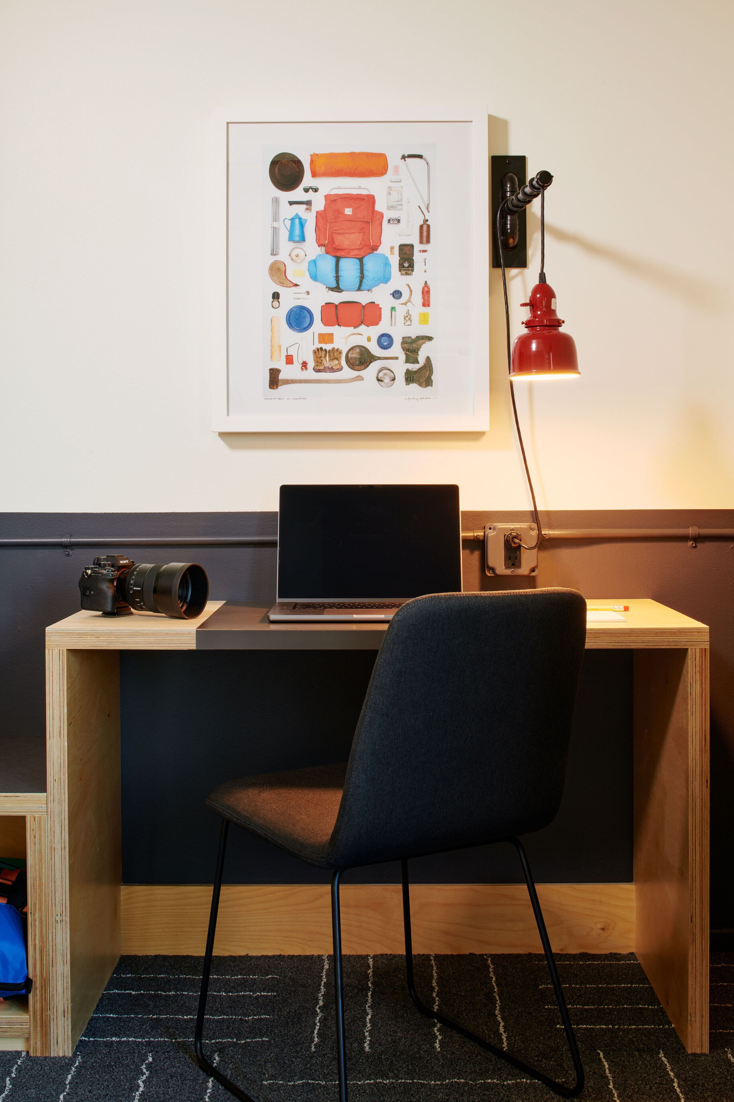 A workspace with a laptop, camera, and a framed illustration on the wall.