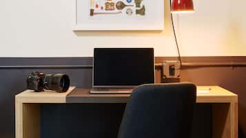 A workspace with a laptop, camera, and a framed illustration on the wall.