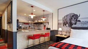 A modern hotel room with a large bed, a red and black checkered throw, a map on the wall, a kitchen area with a bar, and a bull painting. - Mountain Modern Jackson Hole (Jackson)