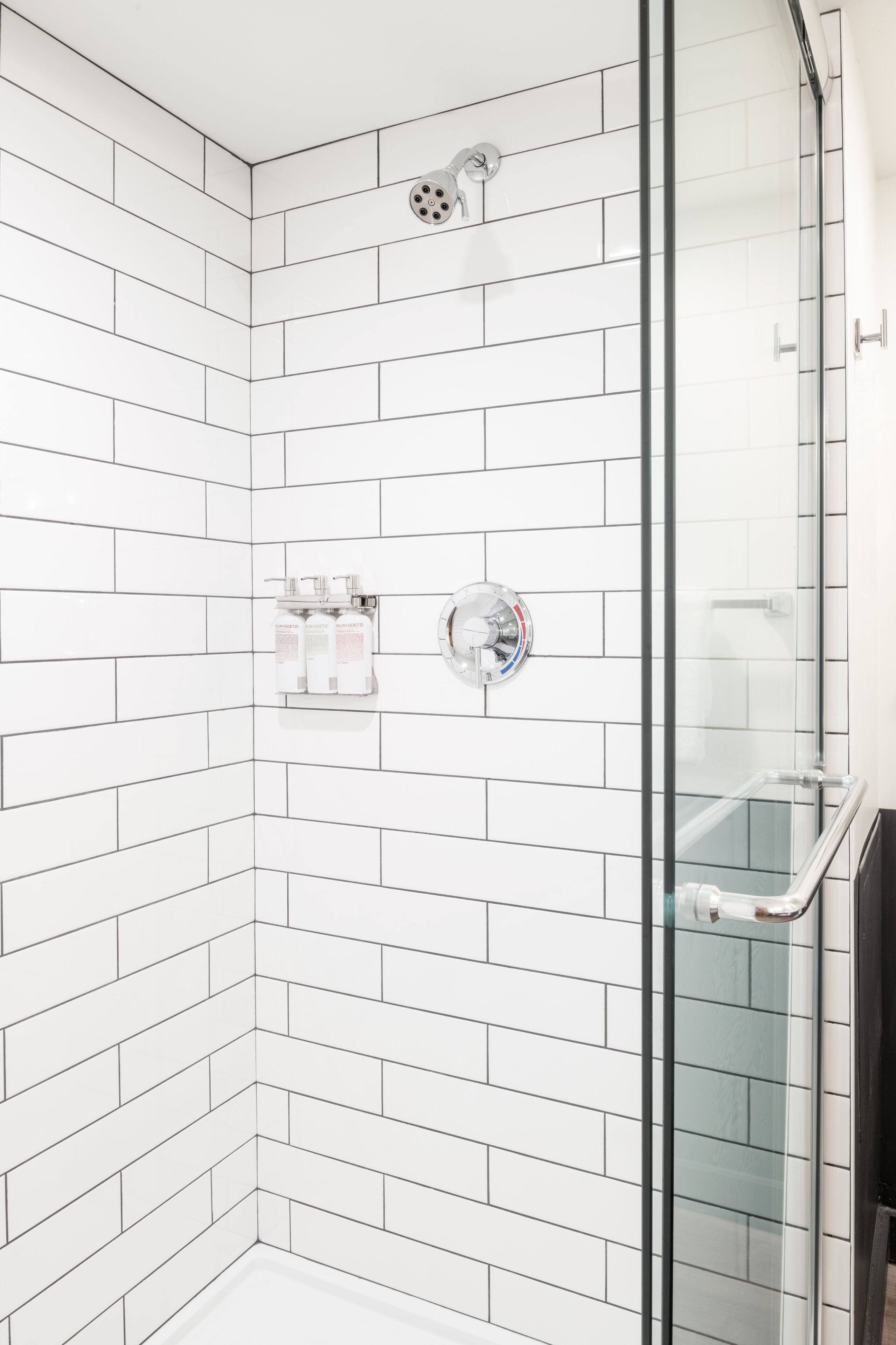 A corner shower with white subway tiles, a glass door, and a hand dryer.