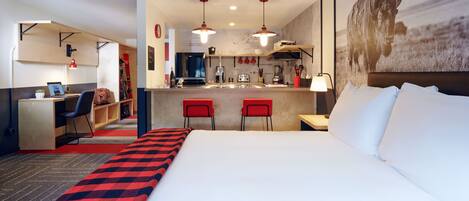 Habitación de hotel con cama, escritorio, silla, kitchenette y una obra de arte grande en la pared.