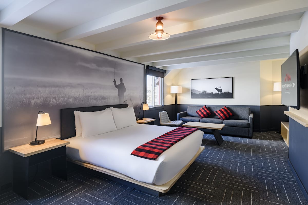 A hotel room with a large bed, a sofa, a desk, and a TV.