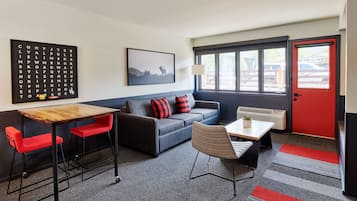 Una habitación moderna con sofá, dos sillas rojas, una mesa de madera, una lámpara y una ventana con vistas a un edificio.