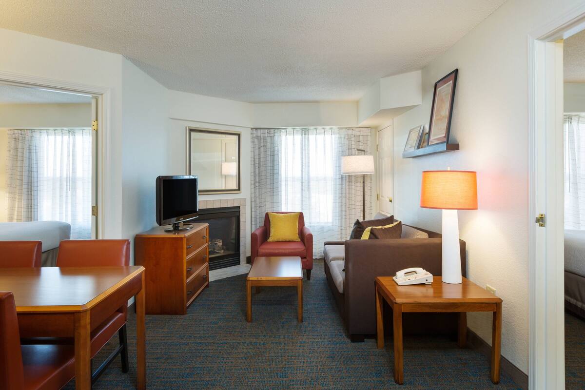 Een hotelkamer met een televisie, een open haard, een bank, een stoel, een tafel en een lamp.