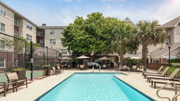 A swimming pool with lounge chairs and umbrellas, surrounded by multi-story buildings with brick and stucco exteriors. - Residence Inn by Marriott Austin Parmer/Tech Ridge (Austin)