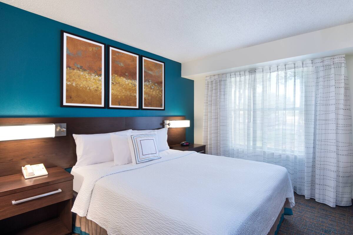 Een hotelkamer met een groot bed, een nachtkastje met een lamp en een kunstwerk aan de muur.