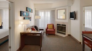 Een hotelkamer met een bed, een bureau met lamp, een stoel, een televisie en een open haard.