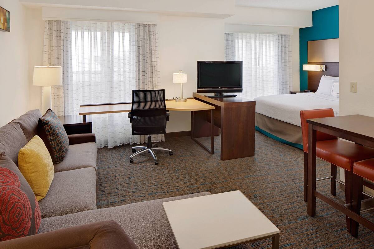 Een hotelkamer met een bed, een bureau met een televisie, een bank en een eettafel.
