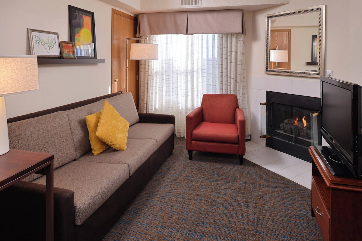 A living room with a sofa, a red armchair, a flat-screen TV, a fireplace, and a patterned carpet.