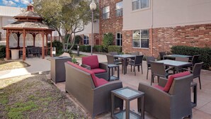 Un espace extérieur aménagé en terrasse, avec des meubles en osier, un belvédère et un bâtiment en briques en arrière-plan.