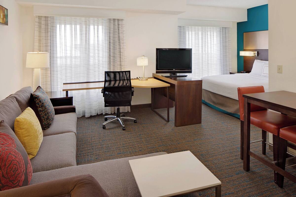 A hotel room with a bed, a desk with a TV, a sofa, and a dining table.
