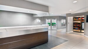 A reception area with a marble counter, a wooden bench, a vending machine, and a glass door leading outside. - Residence Inn by Marriott Greenville-Spartanburg Airport (Greenville)