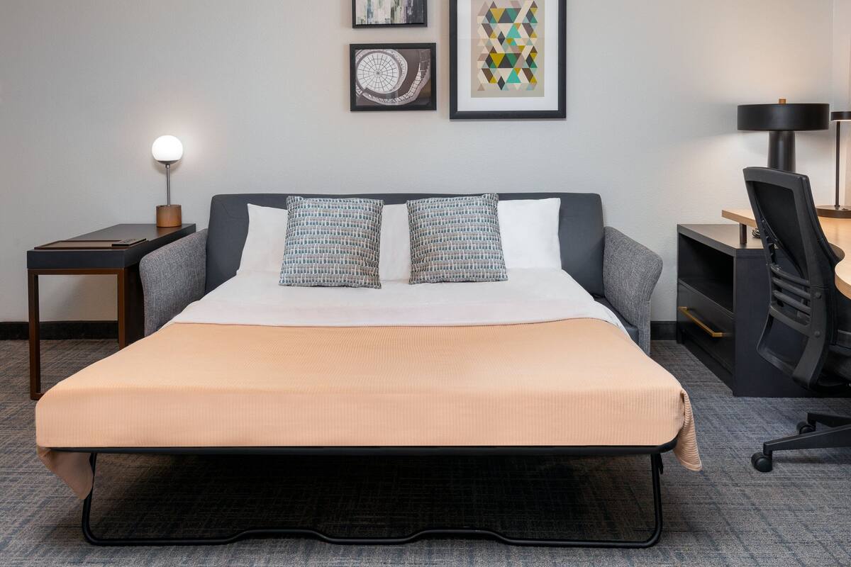 Quarto de hotel bem arrumado, com cama, mesas de cabeceira, escrivaninha e uma cadeira.