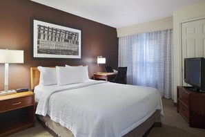 Une chambre d’hôtel avec un grand lit, un bureau avec un ordinateur portable, une télévision et un tableau encadré au mur.