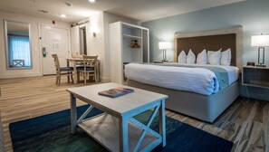 A hotel room with a bed, bedside table, and a desk with chairs. There is a closet with hanging clothes and a window with curtains.