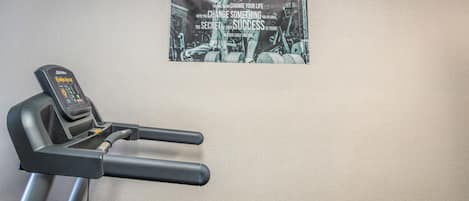 Un gimnasio con una cinta de correr y un cartel motivacional en la pared.