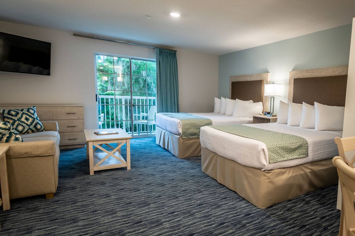 A hotel room with two beds, a sofa, a small table, and a TV.