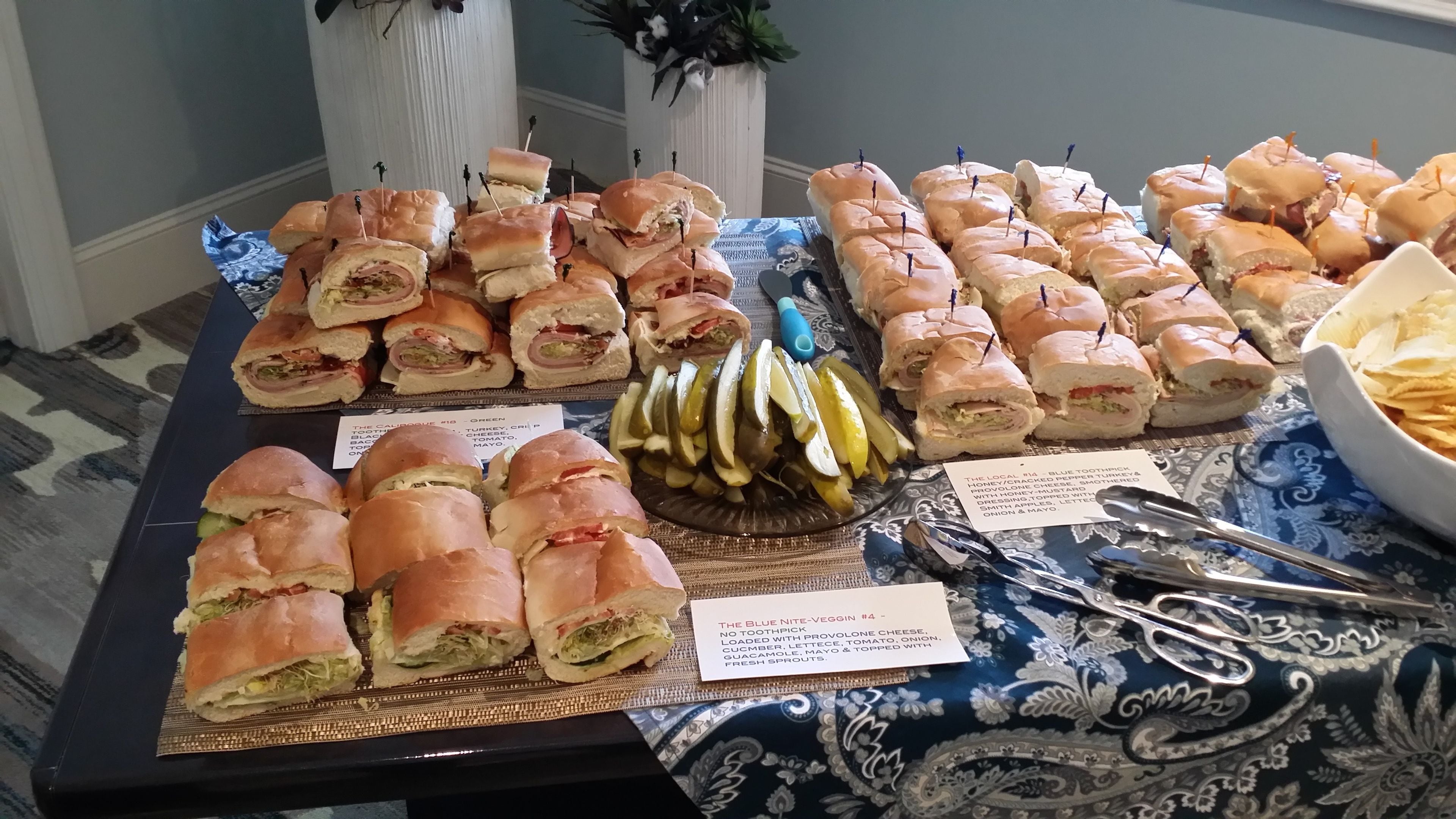 A buffet table with various sandwiches and pickles.
