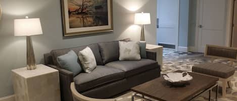 A living room with a grey sofa, two side tables with lamps, a coffee table, and a patterned rug.
