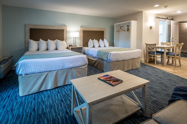 A hotel room with two beds, a small table, a chair, and a desk.