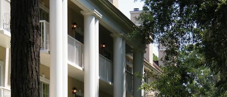 Un edificio con varios balcones y columnas, rodeado de follaje y árboles.