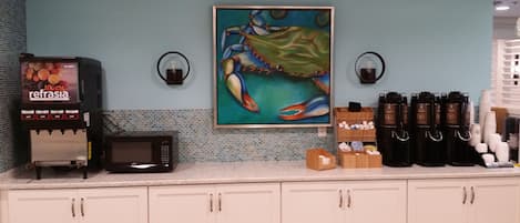 Una kitchenette con cafetera, microondas, un cuadro de cangrejo y dispensadores de café.