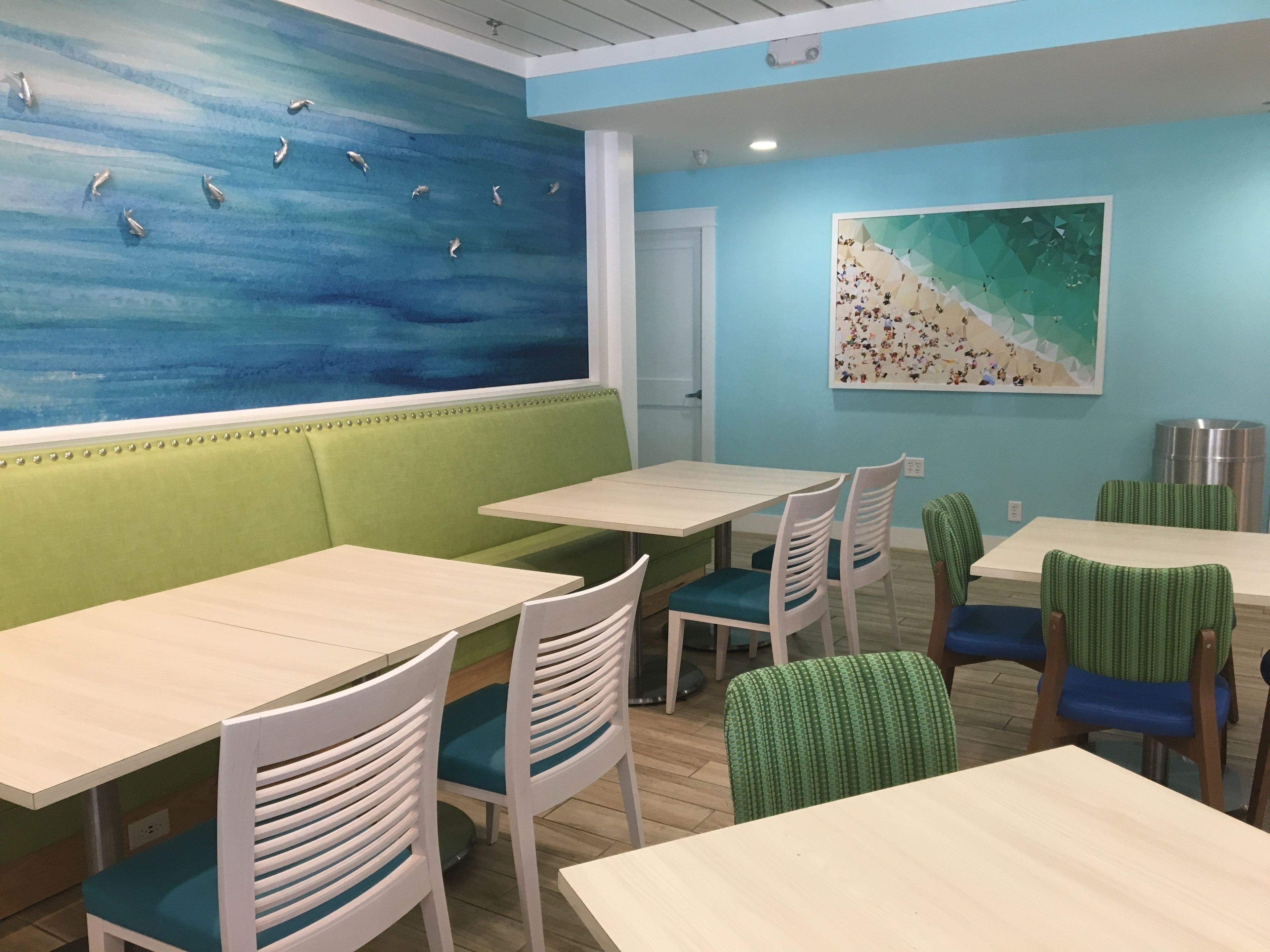 A dining area with green booths, white and green chairs, and a blue wall with a fish mural.