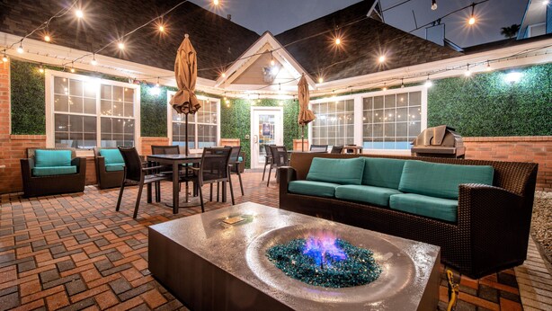 An outdoor patio area with brick flooring, wicker furniture, and a central fire feature. - Residence Inn by Marriott McAllen (McAllen)