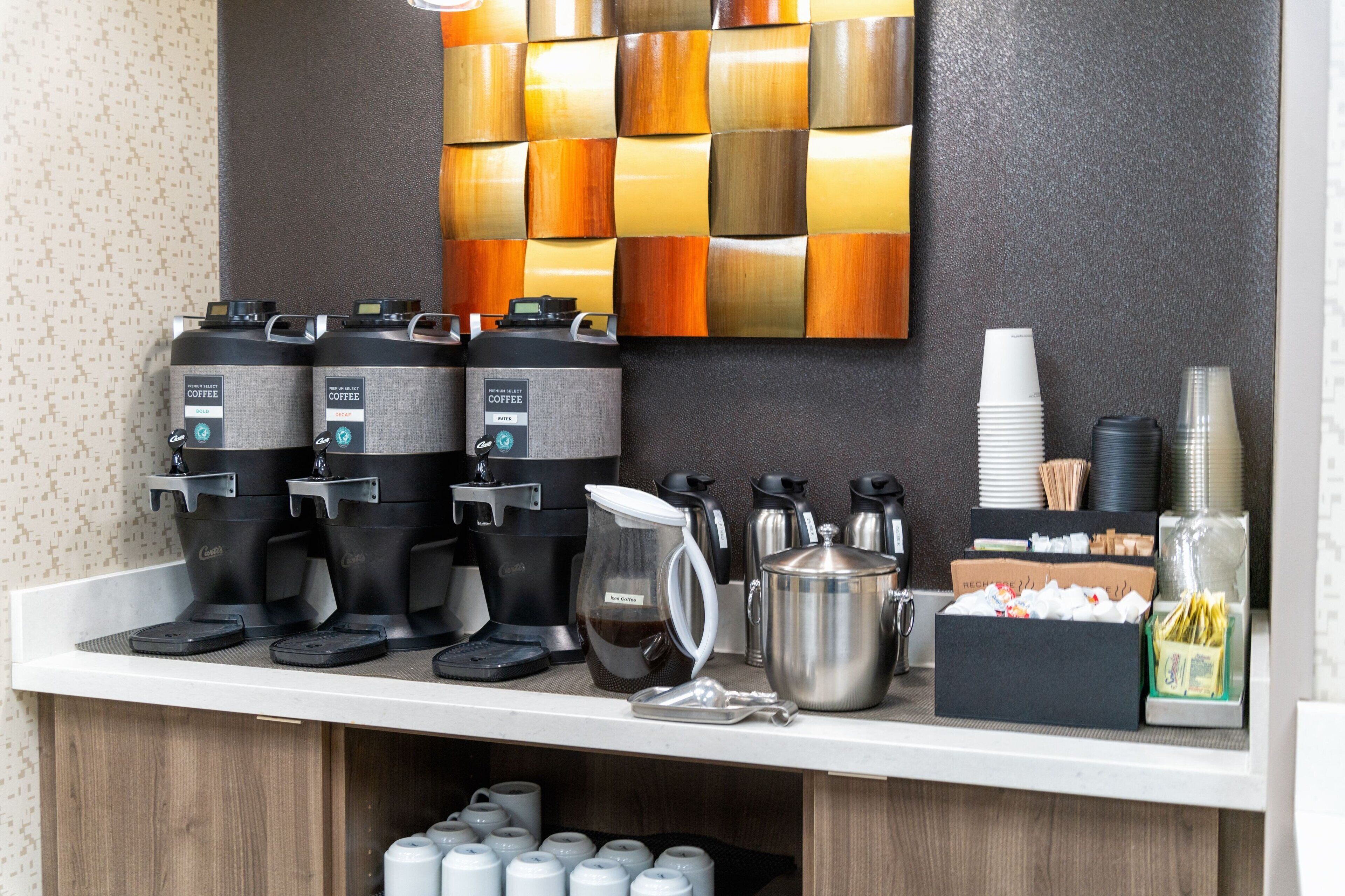 Una estación de café con varias máquinas de café, un hervidor y vasos desechables.