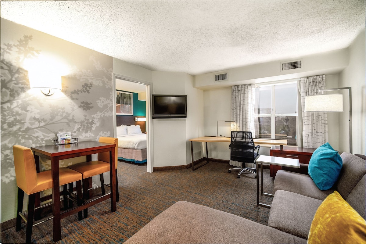 A hotel room with a dining table, a sofa, a desk, and a TV.