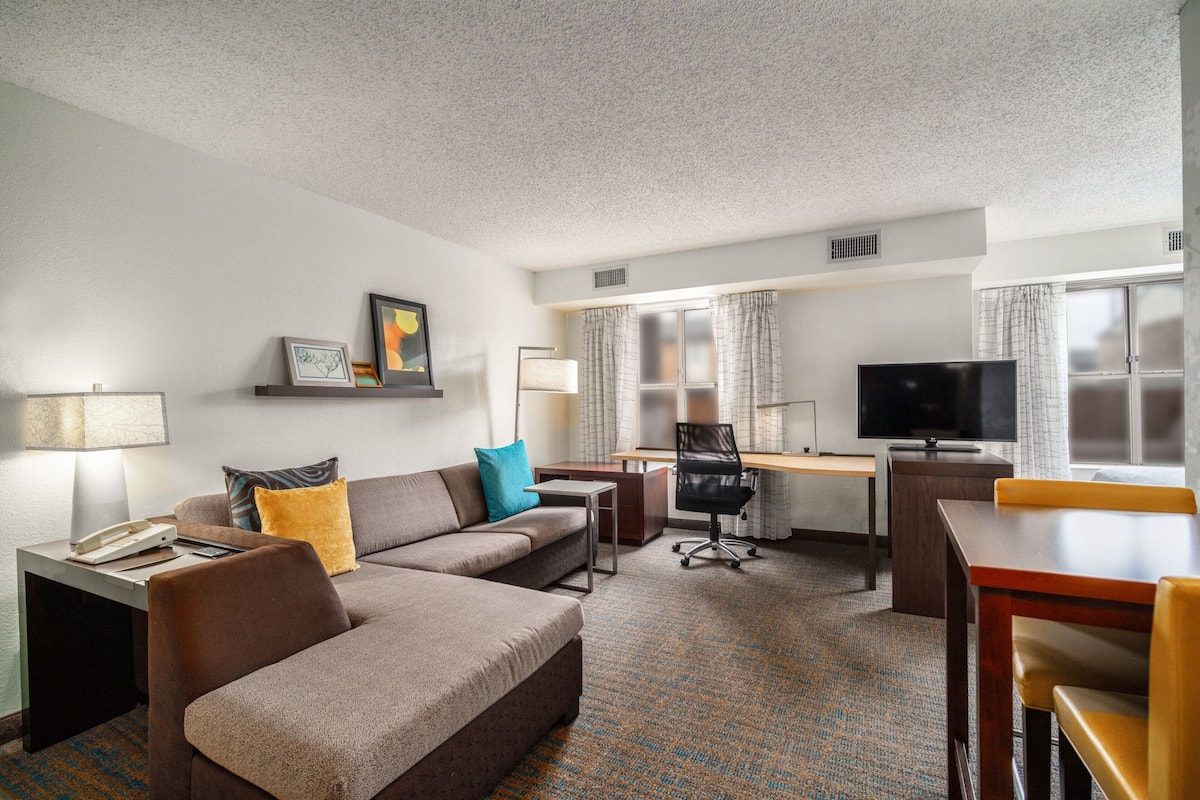 A hotel room with a sofa, a desk, a television, and a lamp.