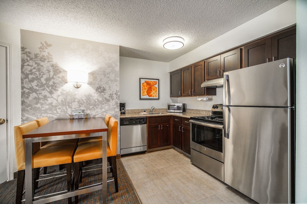 A modern kitchen with stainless steel appliances, wooden cabinets, and a dining area with leather chairs.
